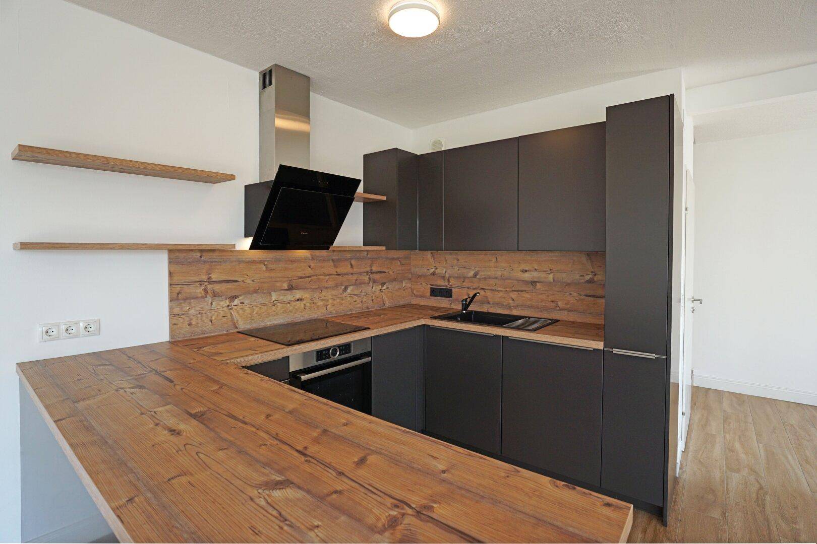 Moderne Einbauküche mit dunklen Schränken, Holz-Arbeitsplatten und integrierten Geräten.