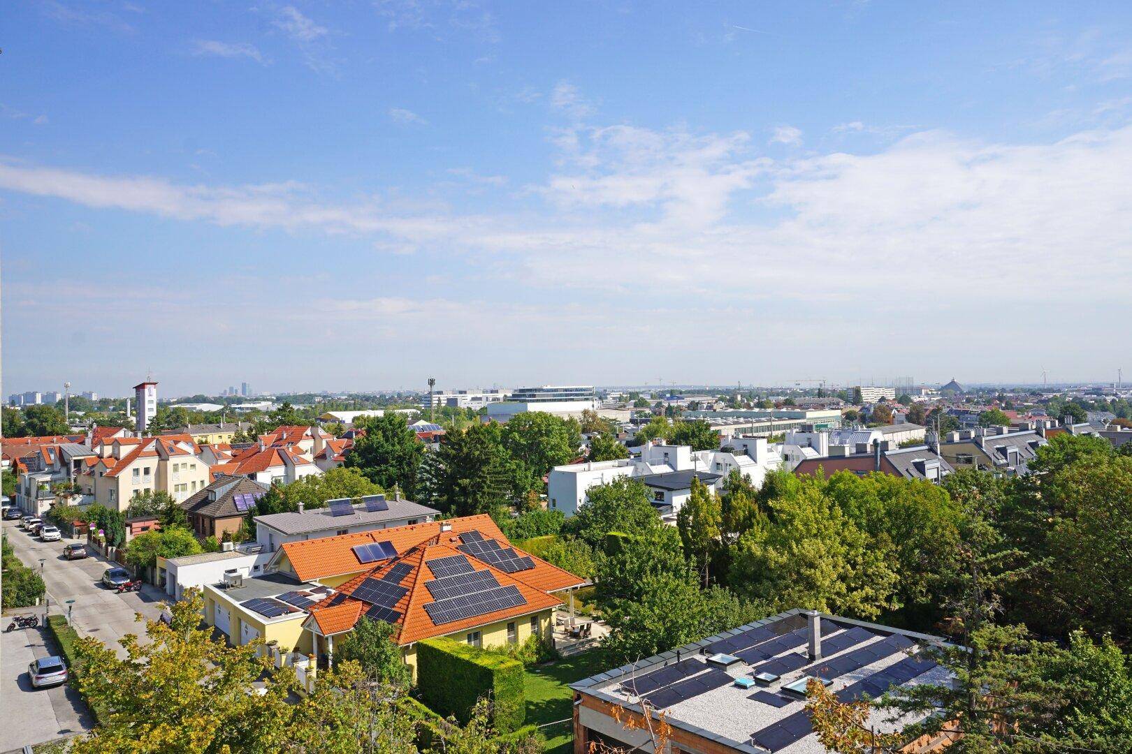 Weitläufiger Blick über die Stadt mit Wohngebäuden und viel Grün unter blauem Himmel.