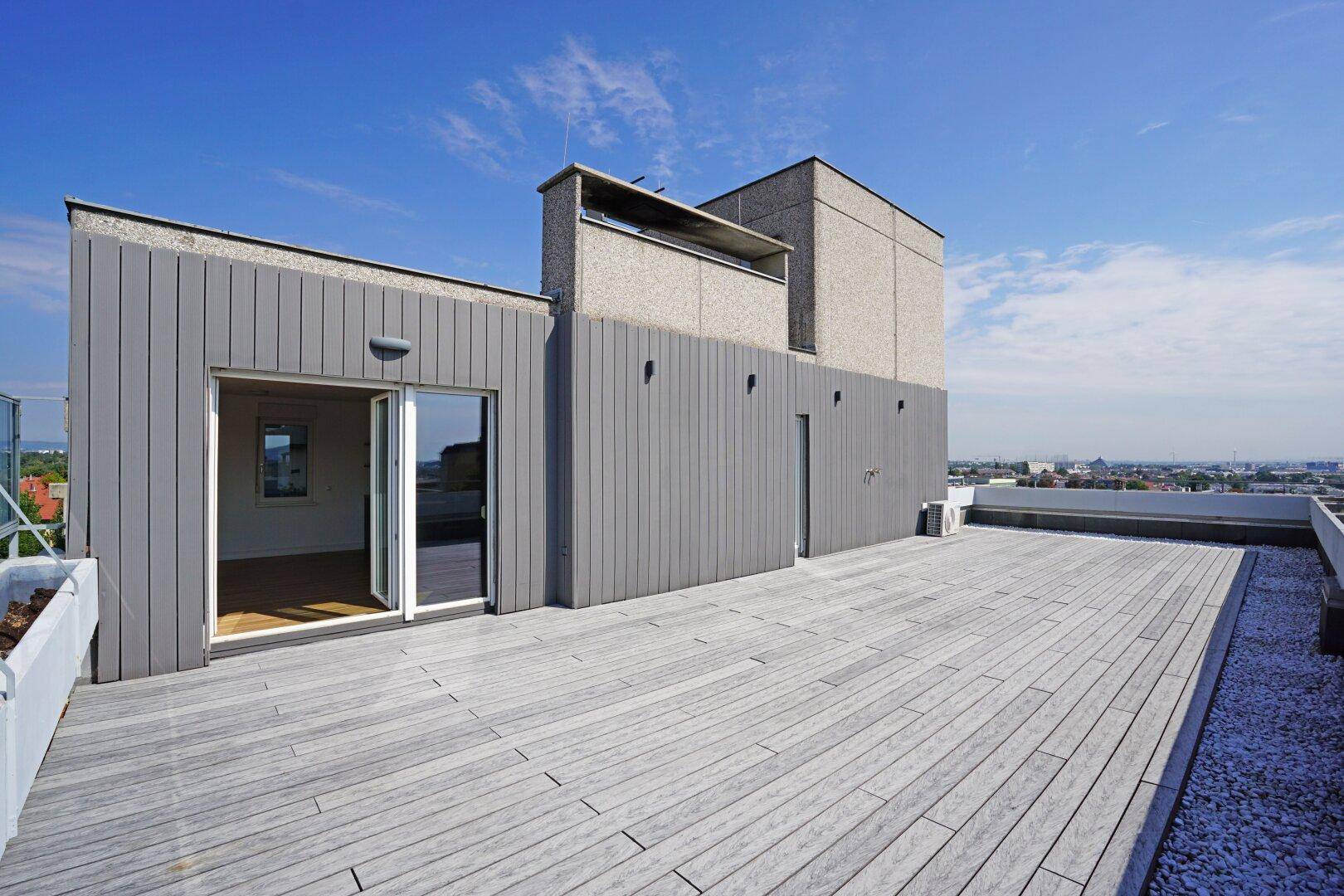 Große Dachterrasse mit Holzbelag und Blick über die Stadt, ideal für Entspannung im Freien.
