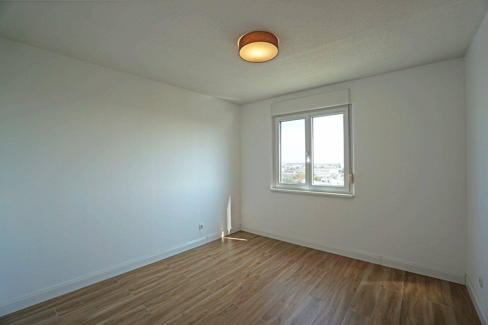 Helles Schlafzimmer mit Holzboden und Fenster, das viel Tageslicht hereinlässt.