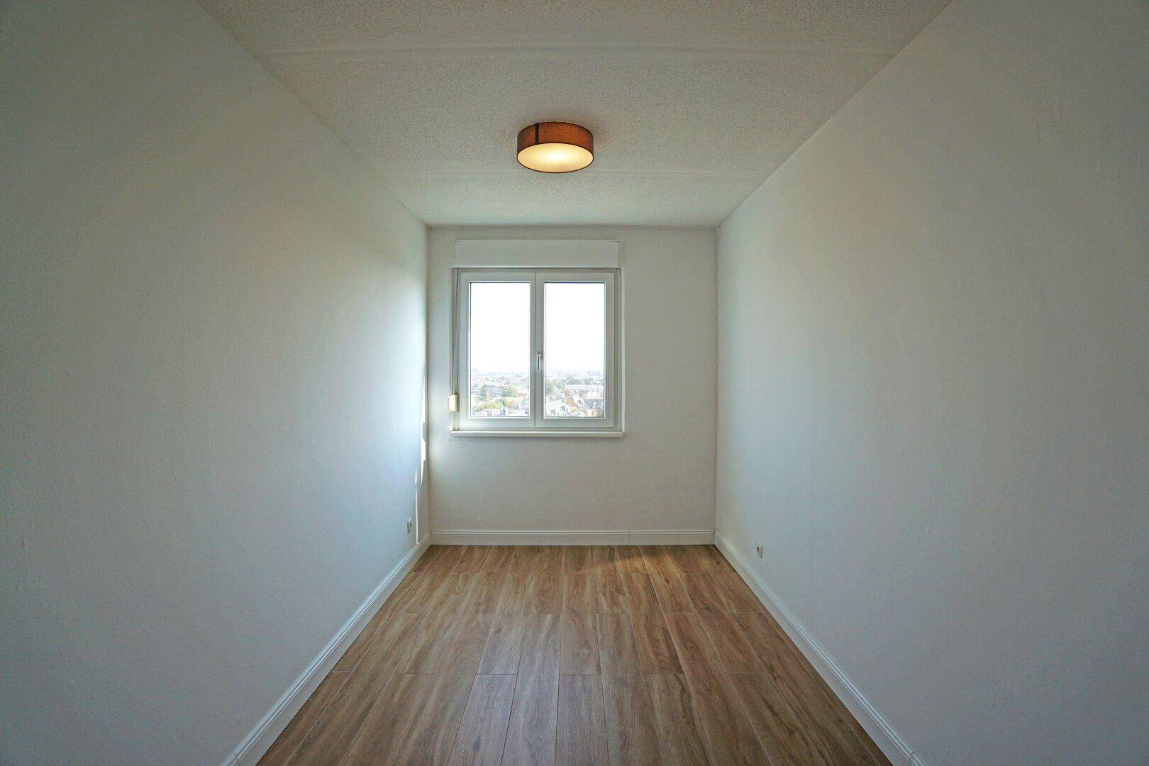 Schlichtes Schlafzimmer mit Holzboden und einem Fenster, das den Raum erhellt.
