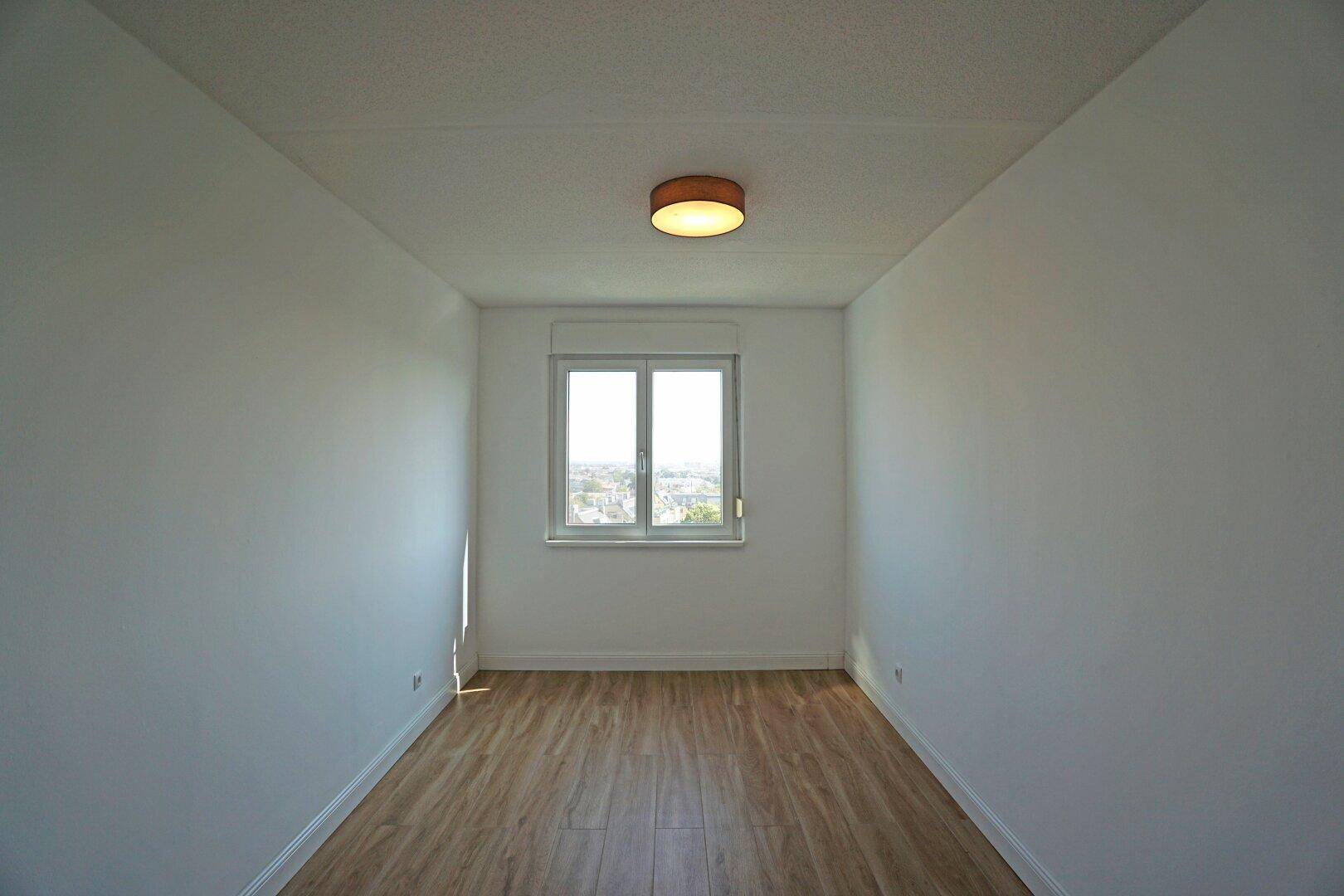 Schlichtes Schlafzimmer mit Holzboden und einem Fenster, das den Raum erhellt.