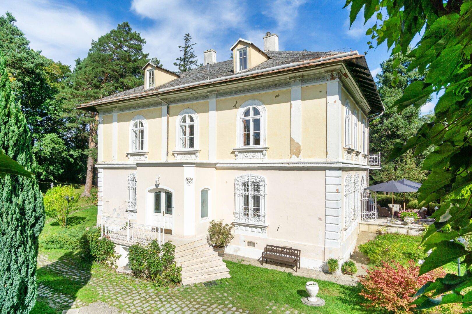 Seitenansicht der historischen Villa mit Terrasse und Treppe, eingebettet in eine grüne Landschaft.