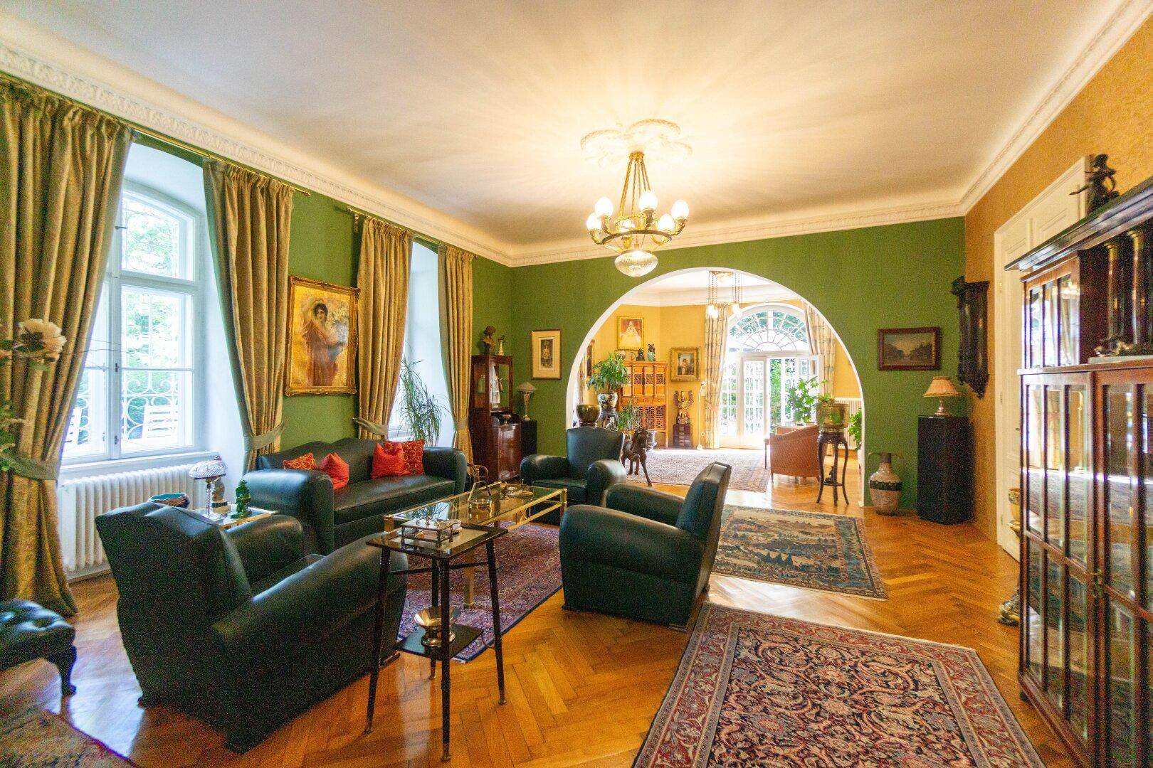 Elegantes Wohnzimmer mit grün gestrichenen Wänden, Fischgrätparkett und klassischen Möbeln.