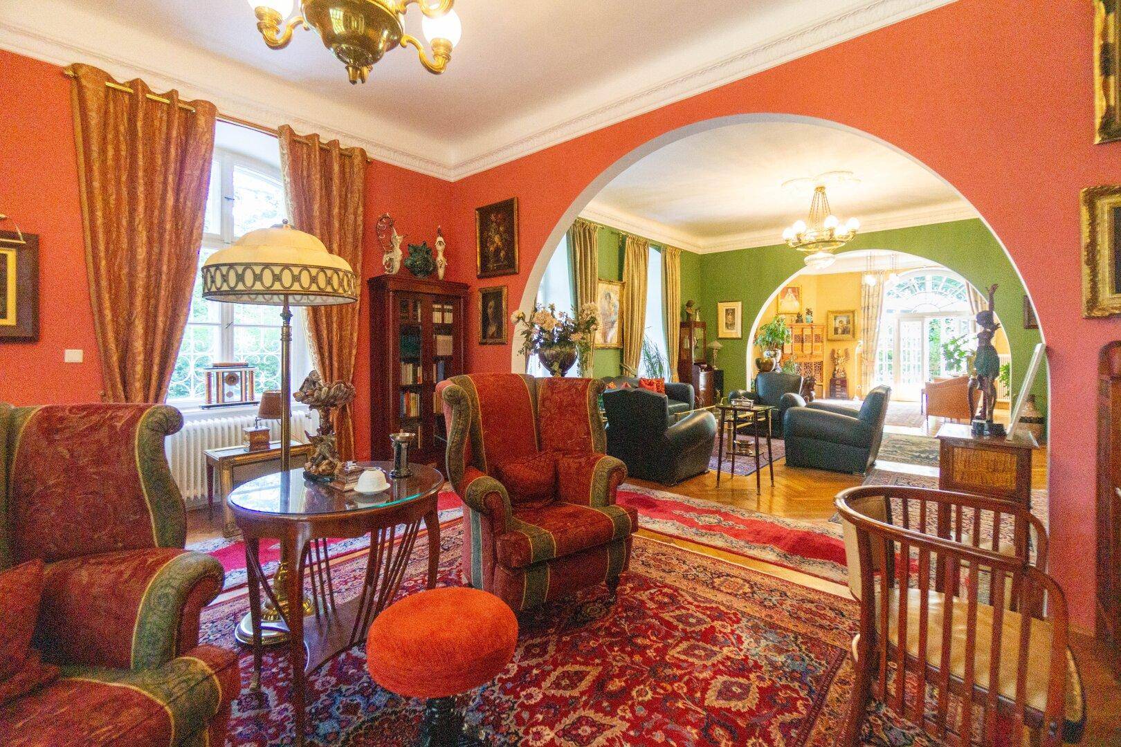 Großzügiges Wohnzimmer mit roten Wänden, klassischen Teppichen und eleganten Sitzmöbeln.