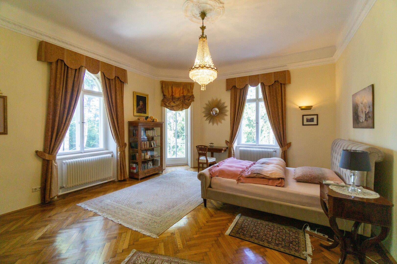 Helles Schlafzimmer mit Parkettboden, klassischem Mobiliar und Blick in den grünen Garten.