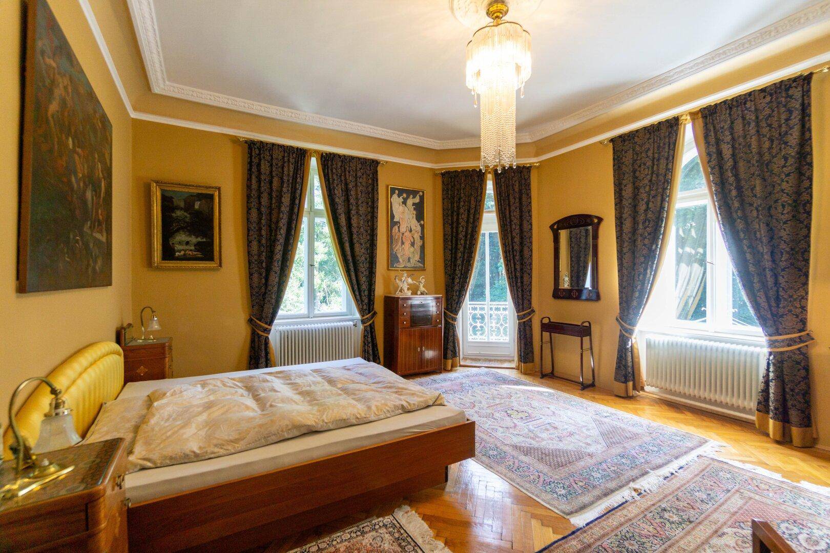 Geräumiges Schlafzimmer mit Parkettboden, großen Fenstern und eleganten Vorhängen, mit Balkonzugang.