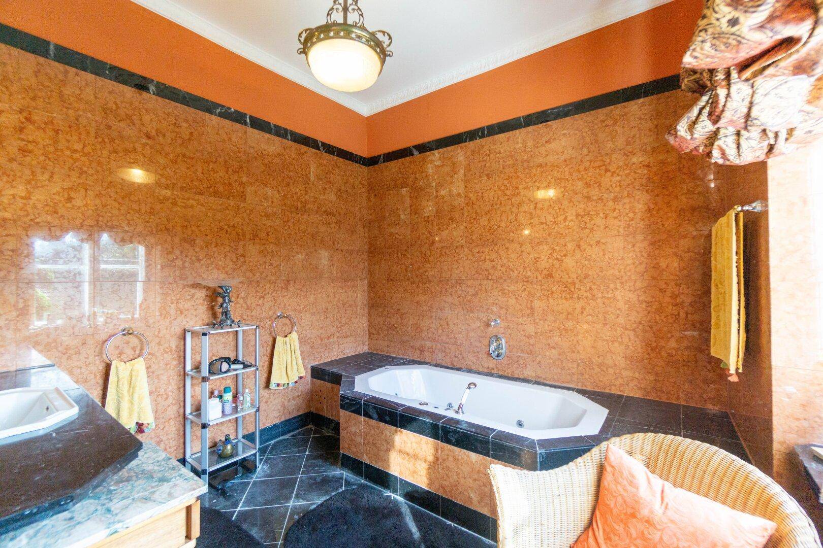 Badezimmer mit braunen Marmorfliesen, dunklem Boden und einer eingebauten Eckbadewanne.