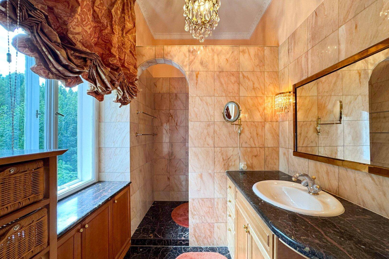 Elegantes Badezimmer mit Marmorfliesen, Waschtisch und großer Dusche, mit Fensterblick ins Grüne.