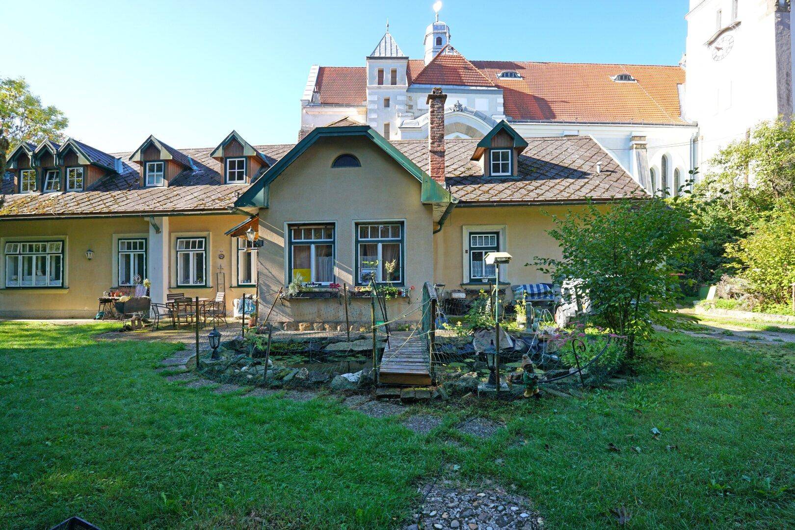 Rückansicht des Hauses mit einem charmanten Garten, kleinem Teich und Blick auf die Kirche.