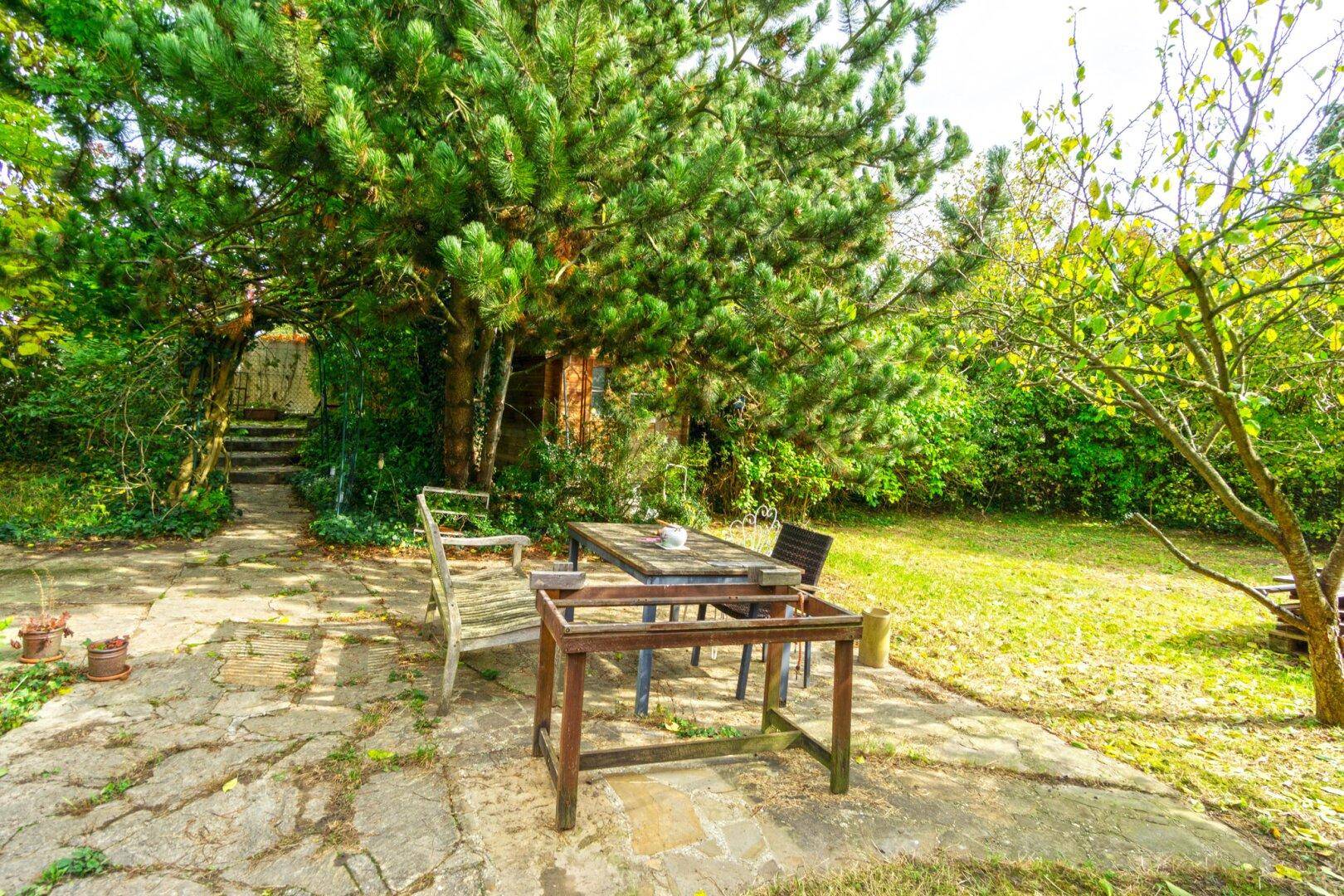Gemütlicher Gartenbereich mit Steinterrasse, Esstisch und umgeben von Bäumen.