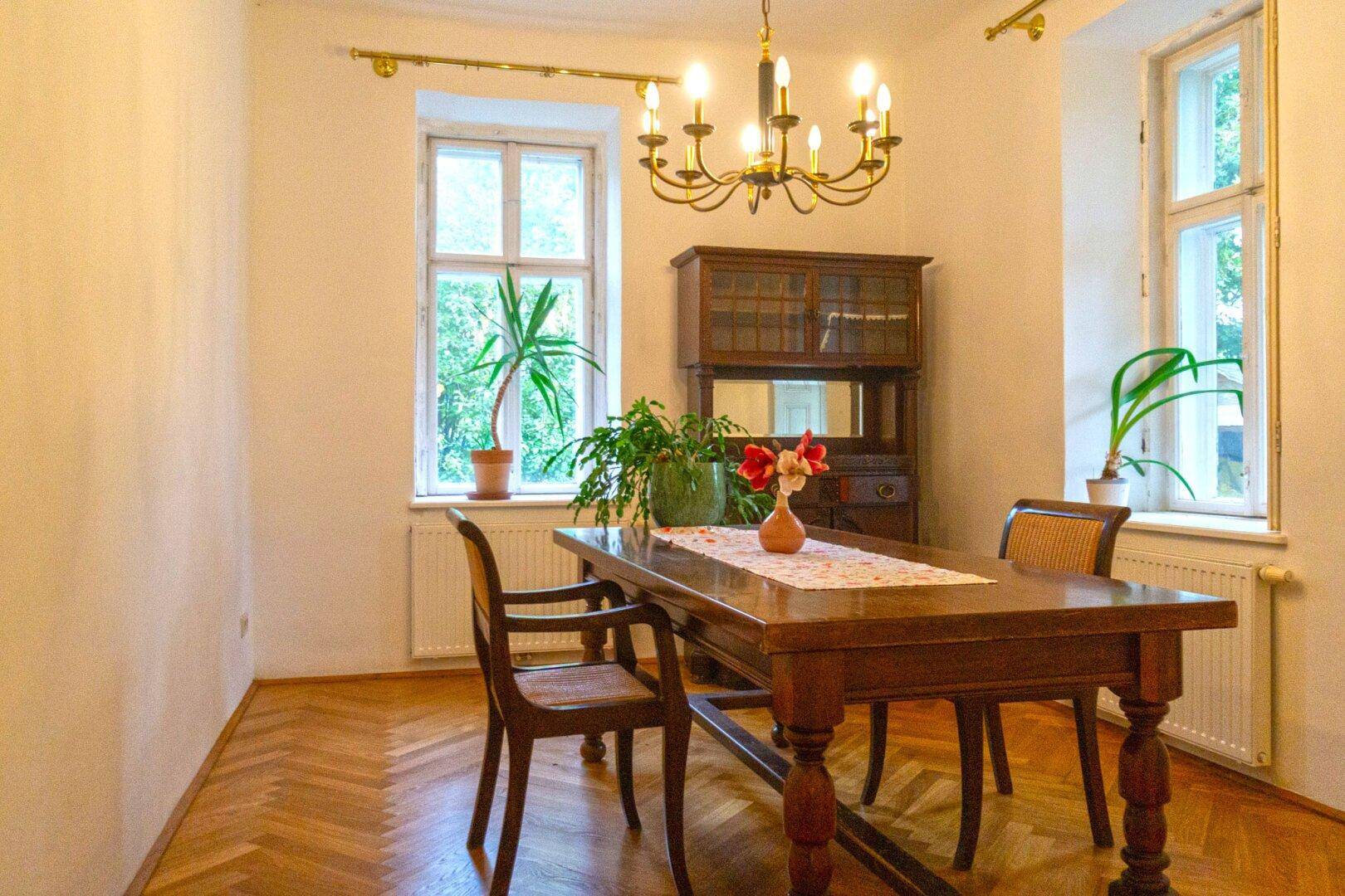 Klassisches Esszimmer mit Holztisch, Kronleuchter und Fischgrätparkett.