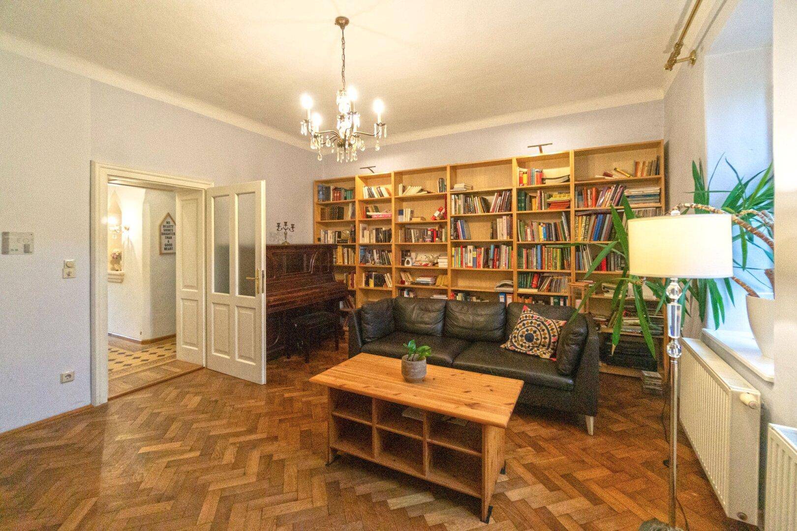 Geräumiges Wohnzimmer mit Bücherregal, Ledersofa und Fischgrätparkett.