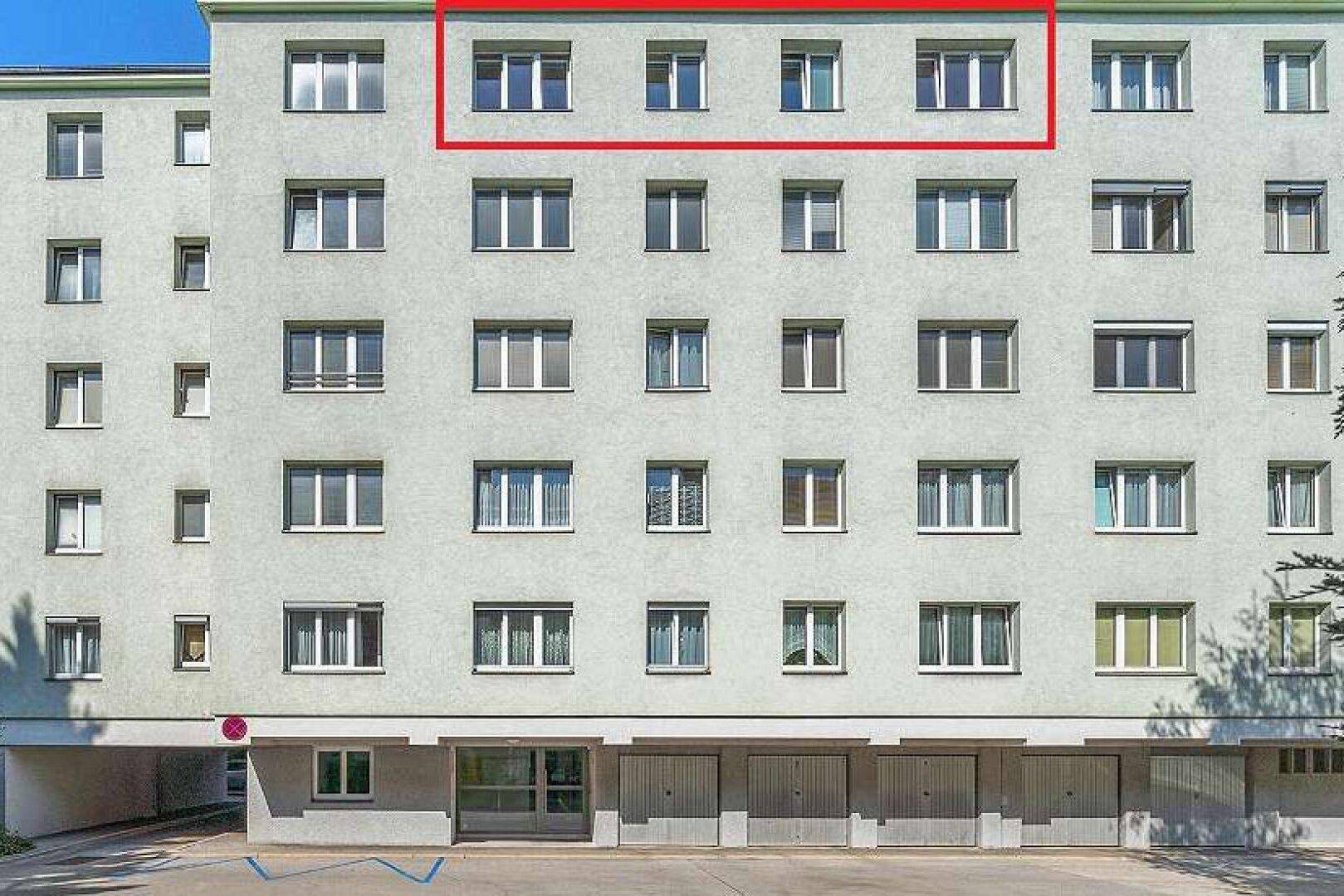 Fassade eines Mehrfamilienhauses mit zahlreichen Fenstern und Garagen im Erdgeschoss, oberste Etage markiert.