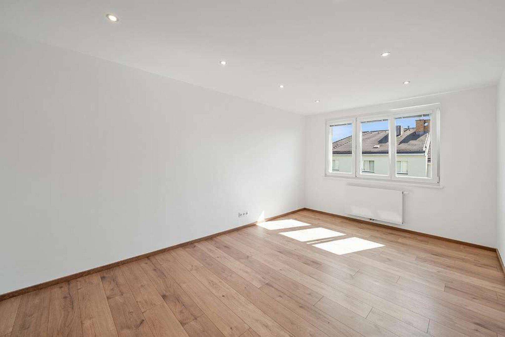 Geräumiger, heller Raum mit Holzboden, weißen Wänden und Einbaustrahlern, ideal als Wohn- oder Schlafzimmer.