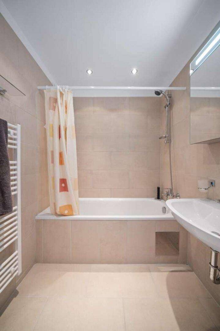 Funktionales Badezimmer mit Badewanne, Duschvorhang, Waschbecken und beheiztem Handtuchhalter.