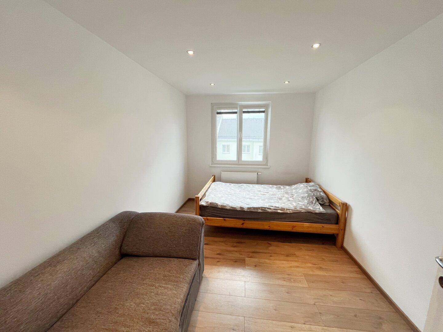 Schlafzimmer mit Holzbett, Sofa, Holzboden und Fenster, bietet eine ruhige und helle Atmosphäre.