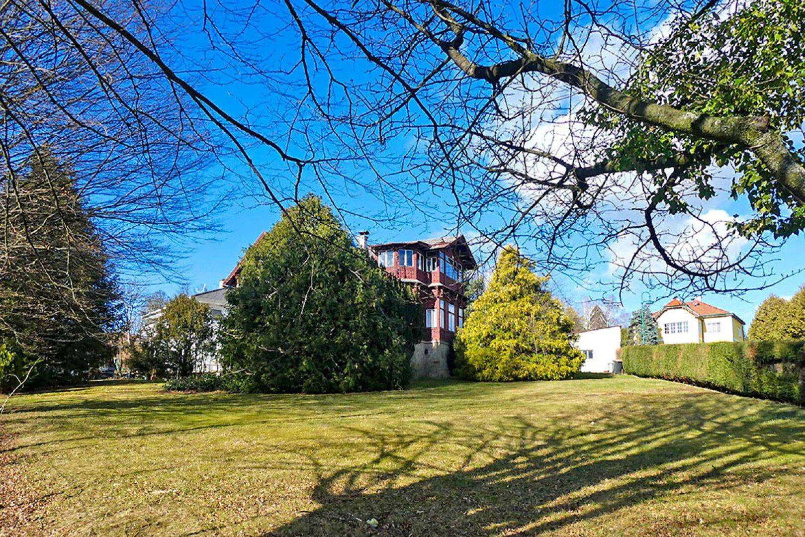 Weitläufige Rasenfläche des Anwesens mit Blick auf die historische Villa und umliegende Bäume.