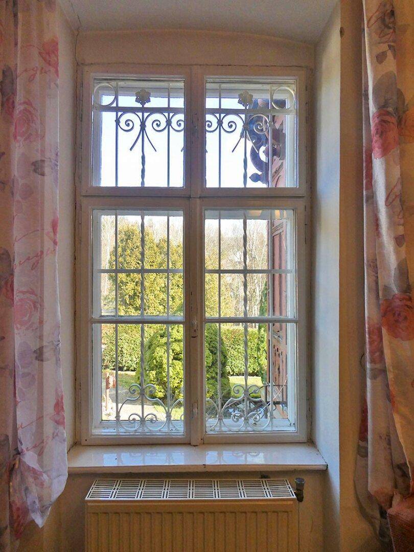 Fenster mit schmiedeeisernem Gitter und Blick auf den grünen Gartenbereich.