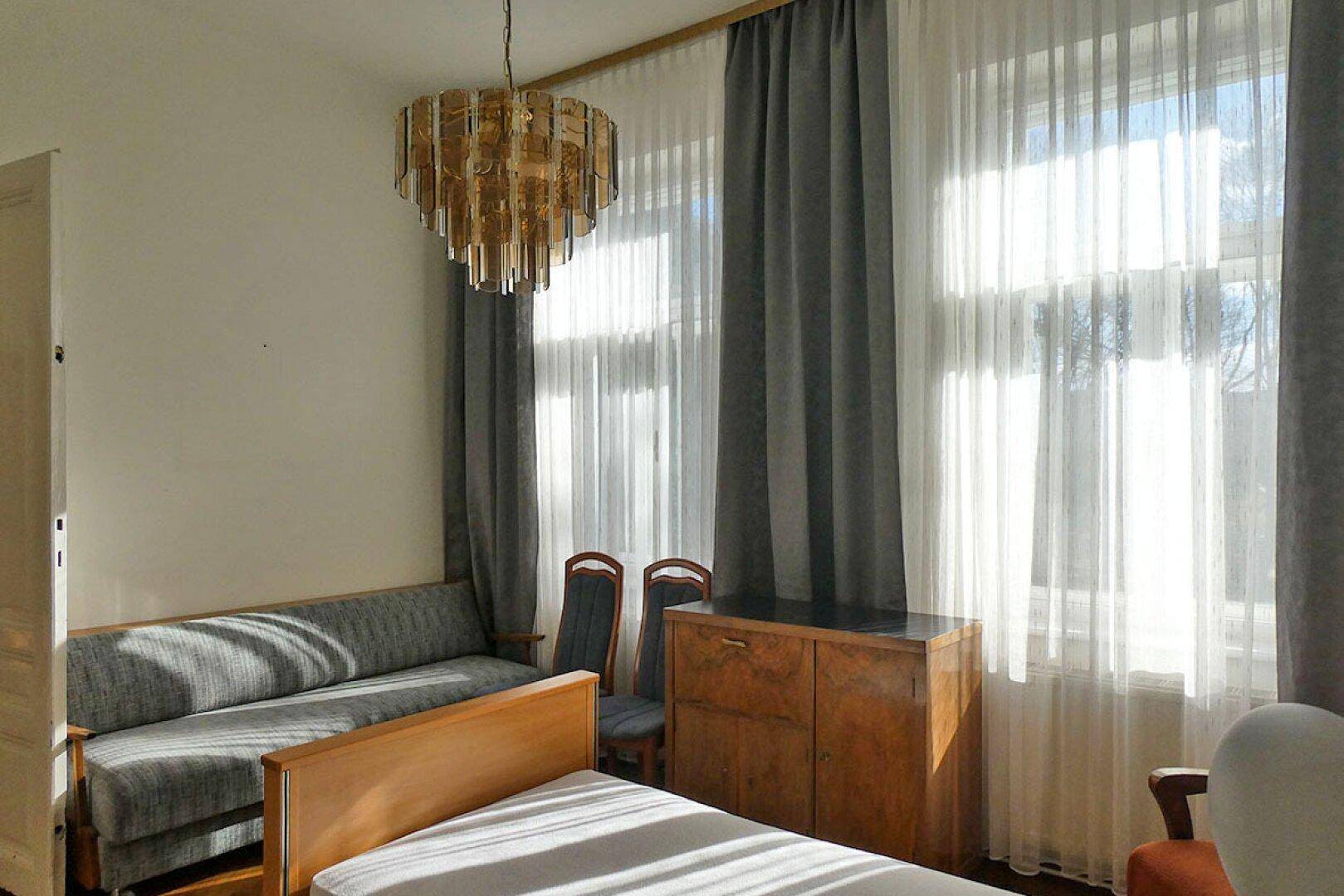 Helles Schlafzimmer mit Einzelbett, Sofa und klassischem Kronleuchter.