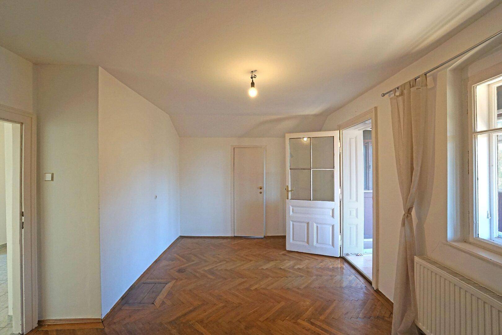 Leerer Raum mit Fischgrätparkett, weißen Wänden und Zugang zu weiteren Zimmern.