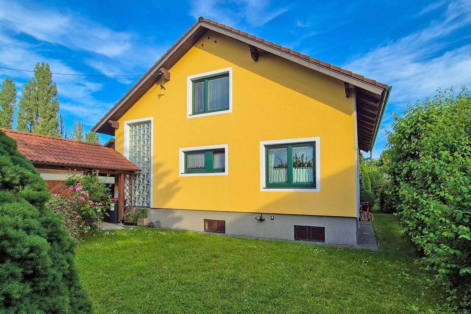 Seitenansicht des gelben Hauses mit grünem Rasen und Bäumen unter blauem Himmel.