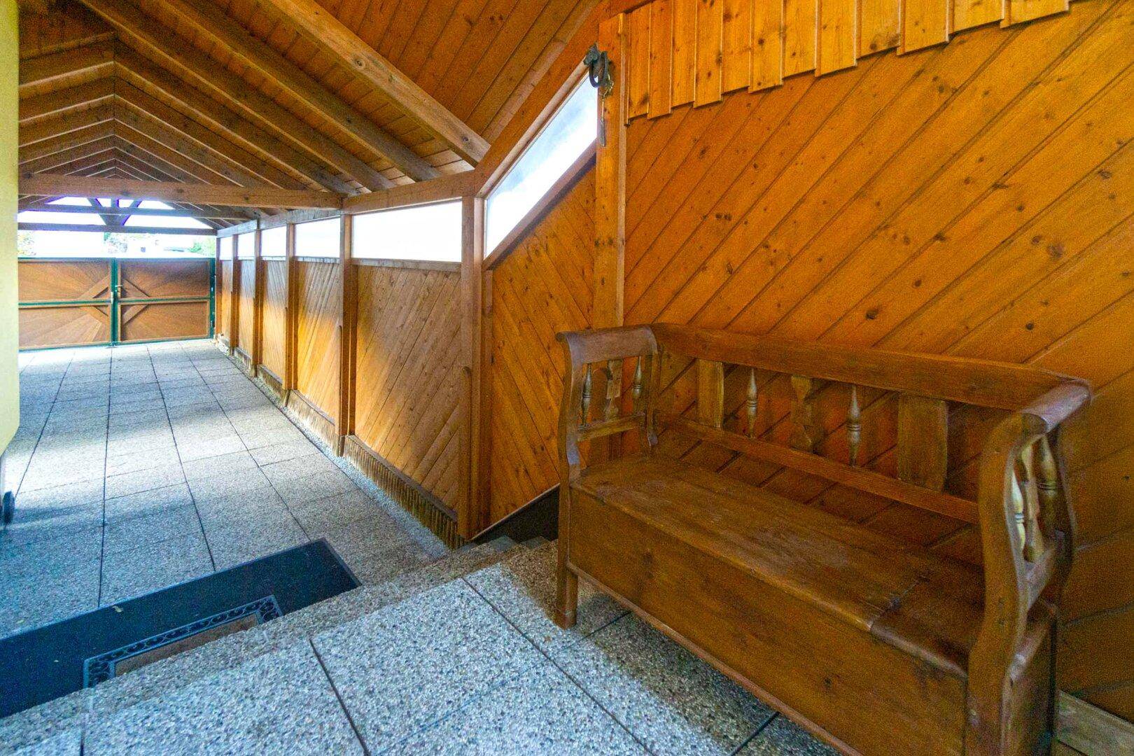 Überdachter Eingangsbereich mit Holzverkleidung, Fliesenboden und einer traditionellen Holzbank.