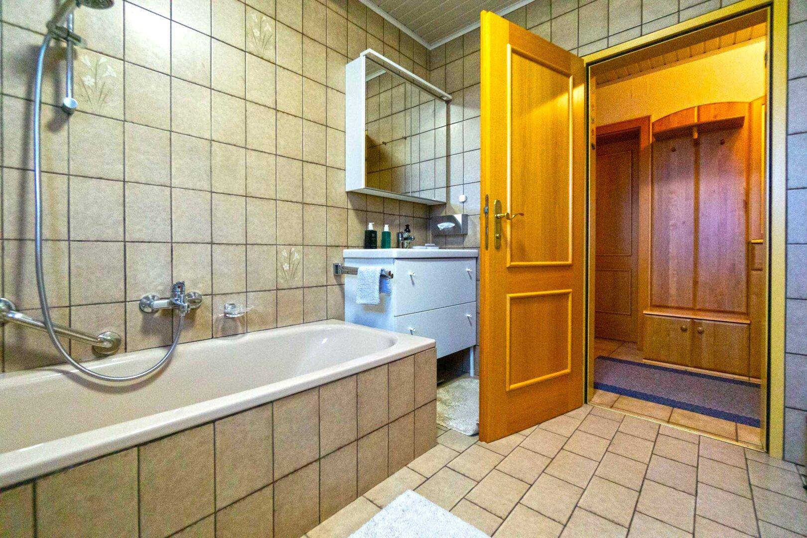 Gefliestes Badezimmer im 80er-Jahre-Stil mit Badewanne, Waschbecken und Spiegelschrank.