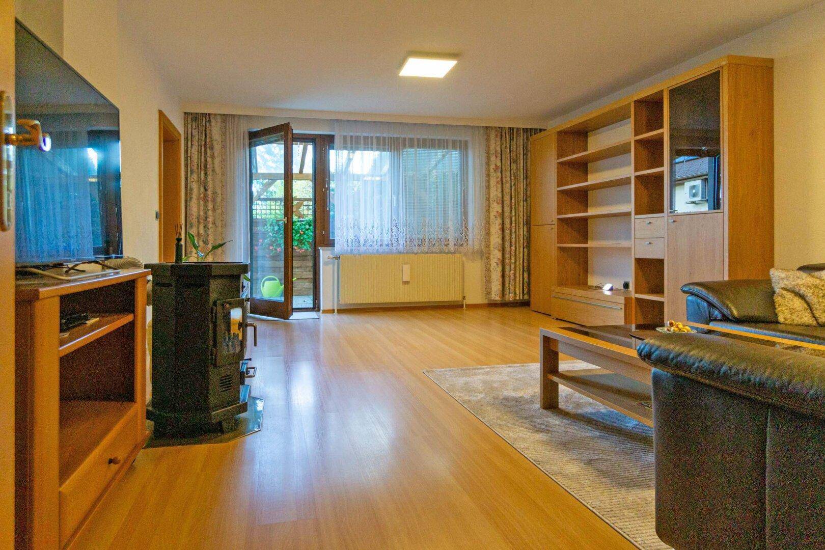 Helles Wohnzimmer mit Holzboden, Kaminofen und Zugang zur Terrasse.