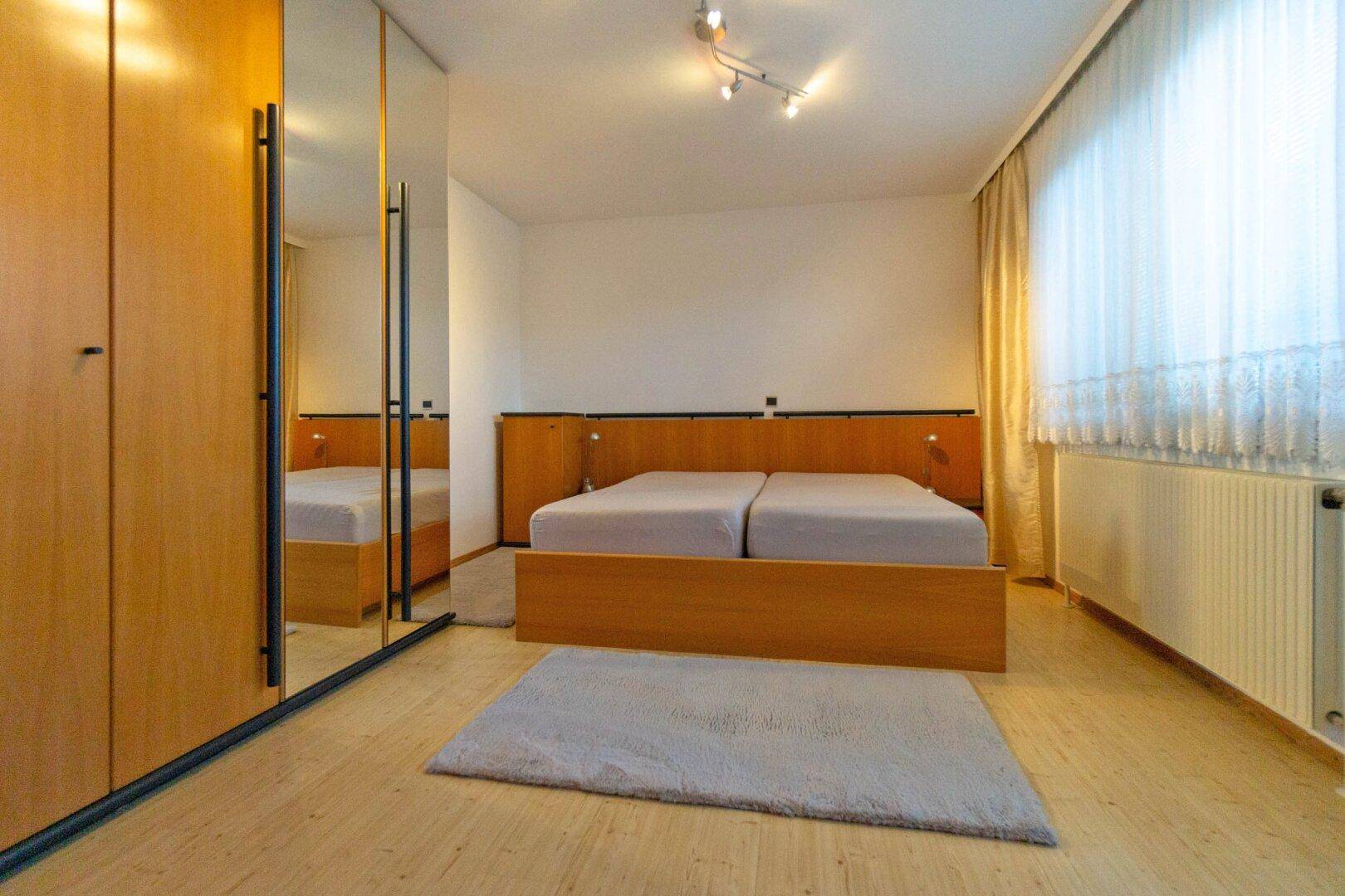 Schlafzimmer mit Holzfußboden, Spiegelschränken und Doppelbett.