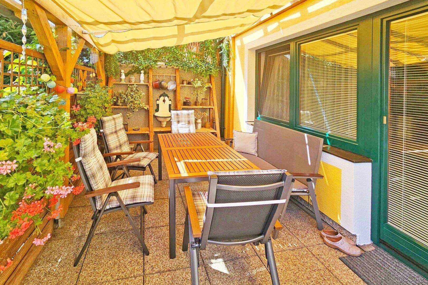 Überdachte Terrasse mit Gartenmöbeln, Pflanzen und Sonnenschutz für entspannte Stunden.