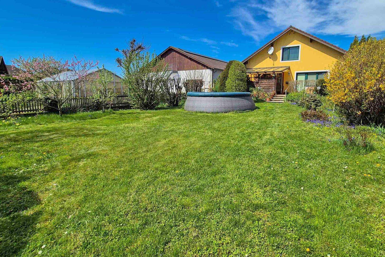 Großer grüner Garten mit Rasenfläche und einem Aufstellpool unter blauem Himmel.