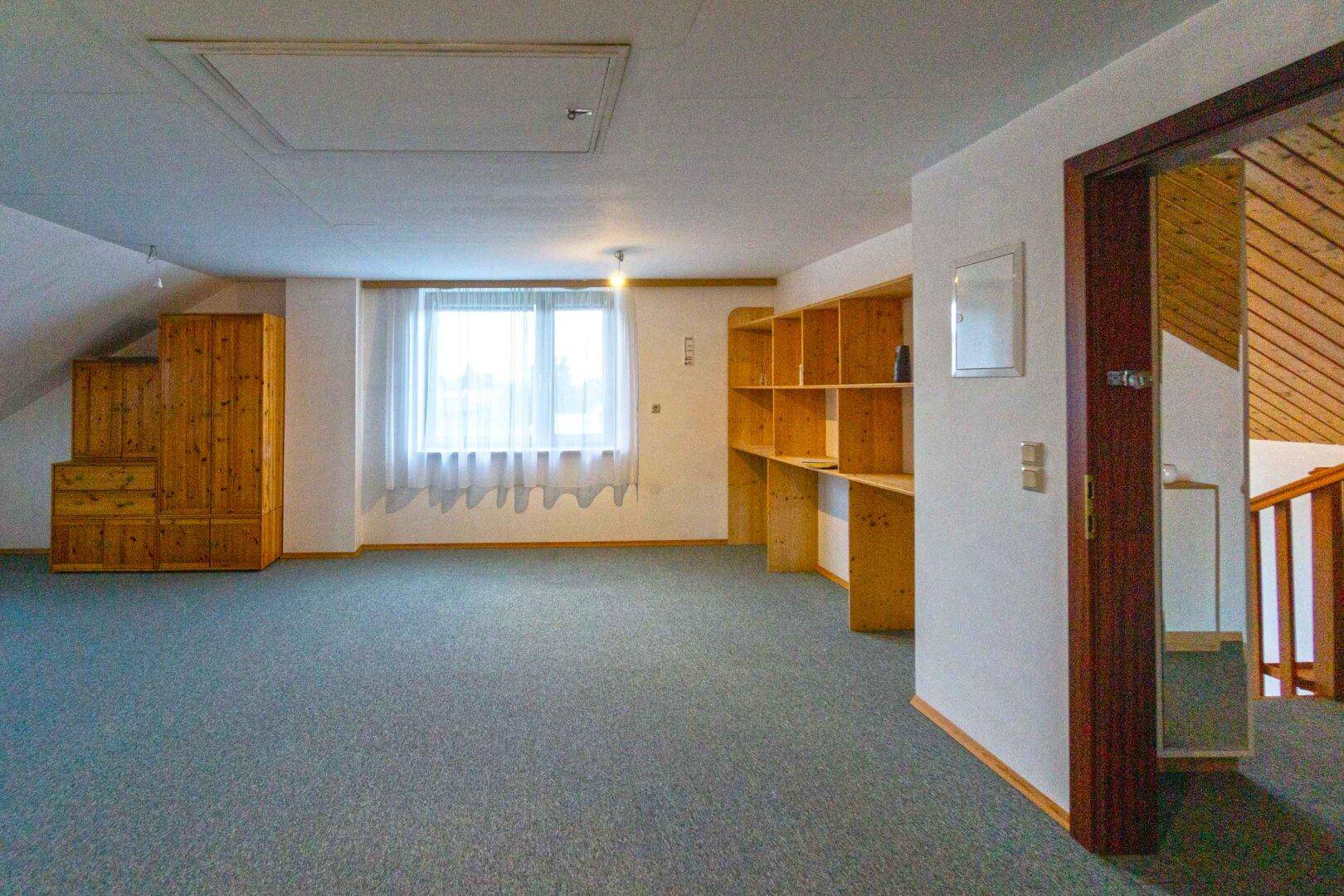 Geräumiger Dachbodenraum mit Teppichboden, Holzregalen und Fenster für viel Tageslicht.