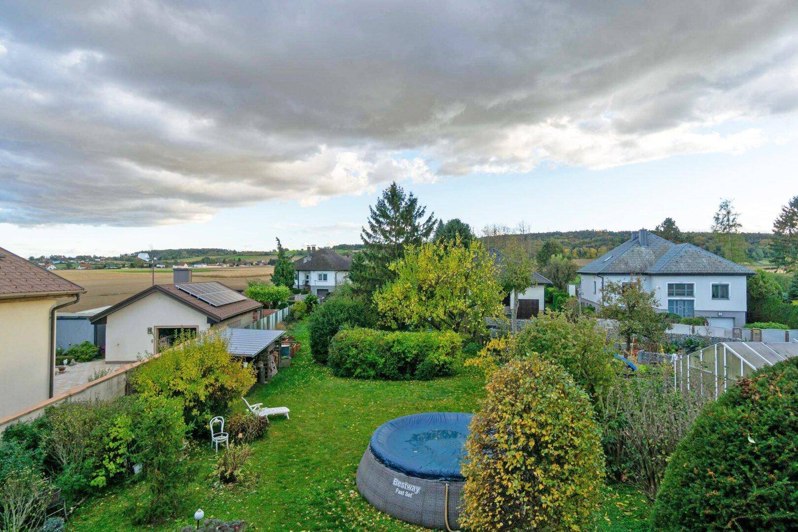Weitläufiger Garten mit Pool und Blick auf die umliegende Landschaft unter bewölktem Himmel.