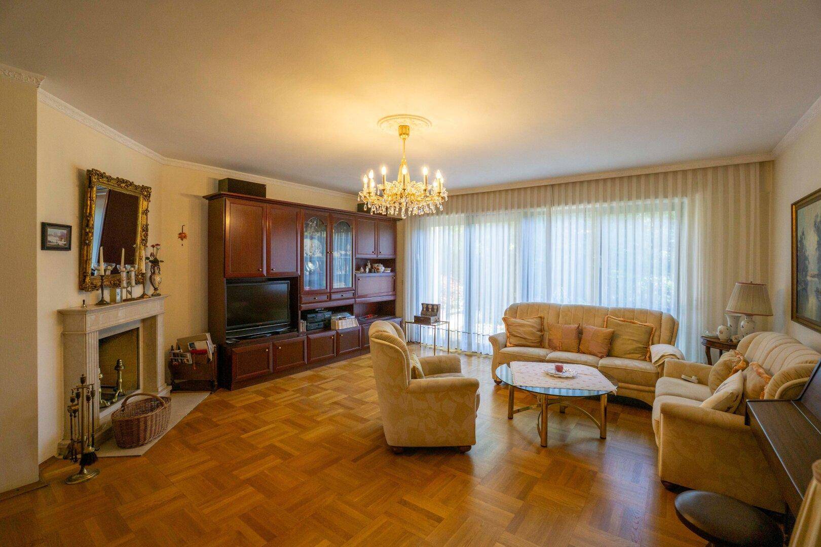 Geräumiges Wohnzimmer mit Parkettboden, Kamin und großen Fenstern zum Garten.
