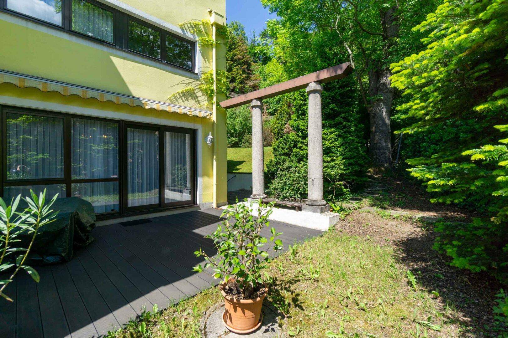 Terrasse mit Holzboden, dekorativen Säulen und direktem Zugang zum Garten.