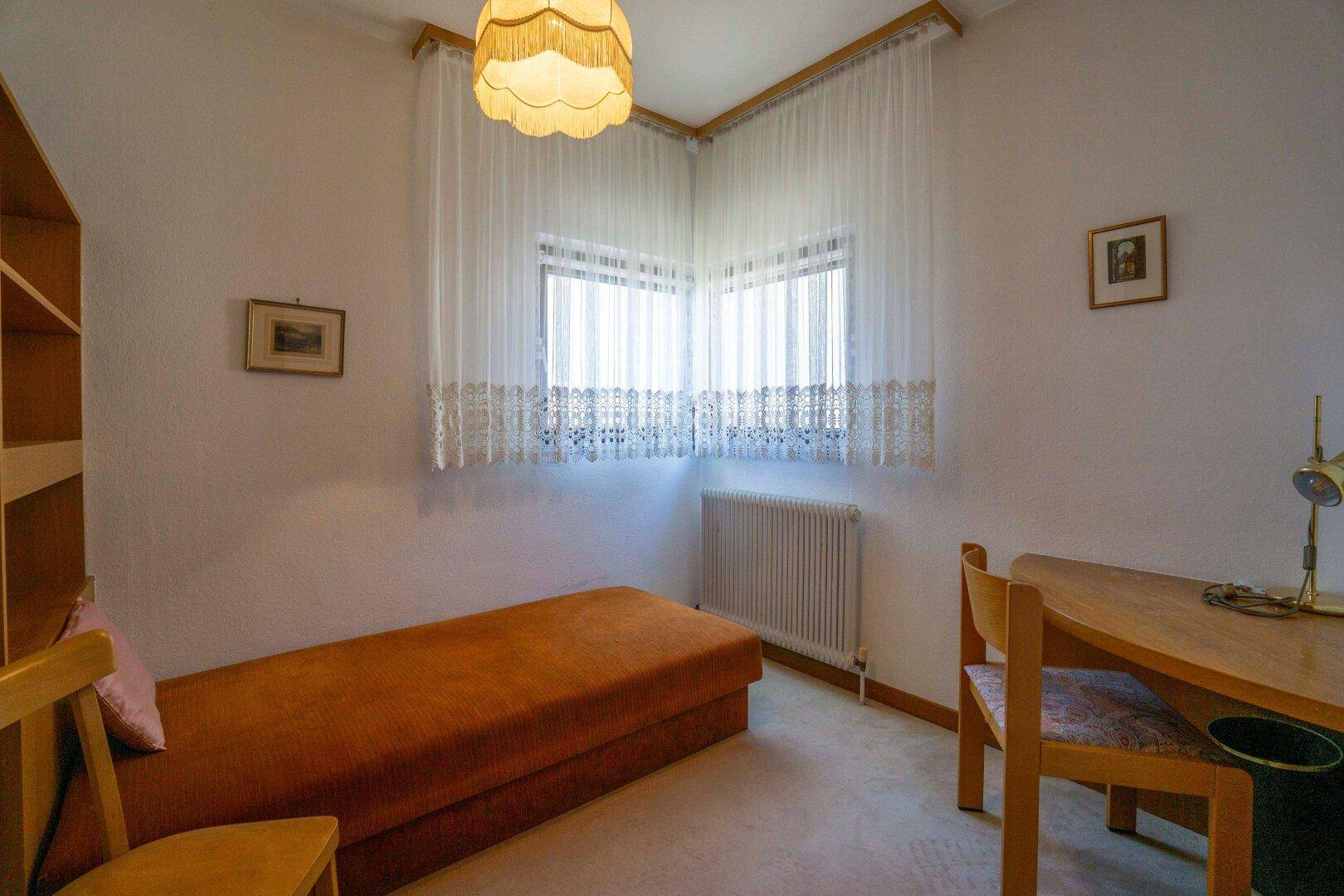 Gemütliches Schlafzimmer mit Einzelbett, Schreibtisch und Eckfenstern für viel Licht.