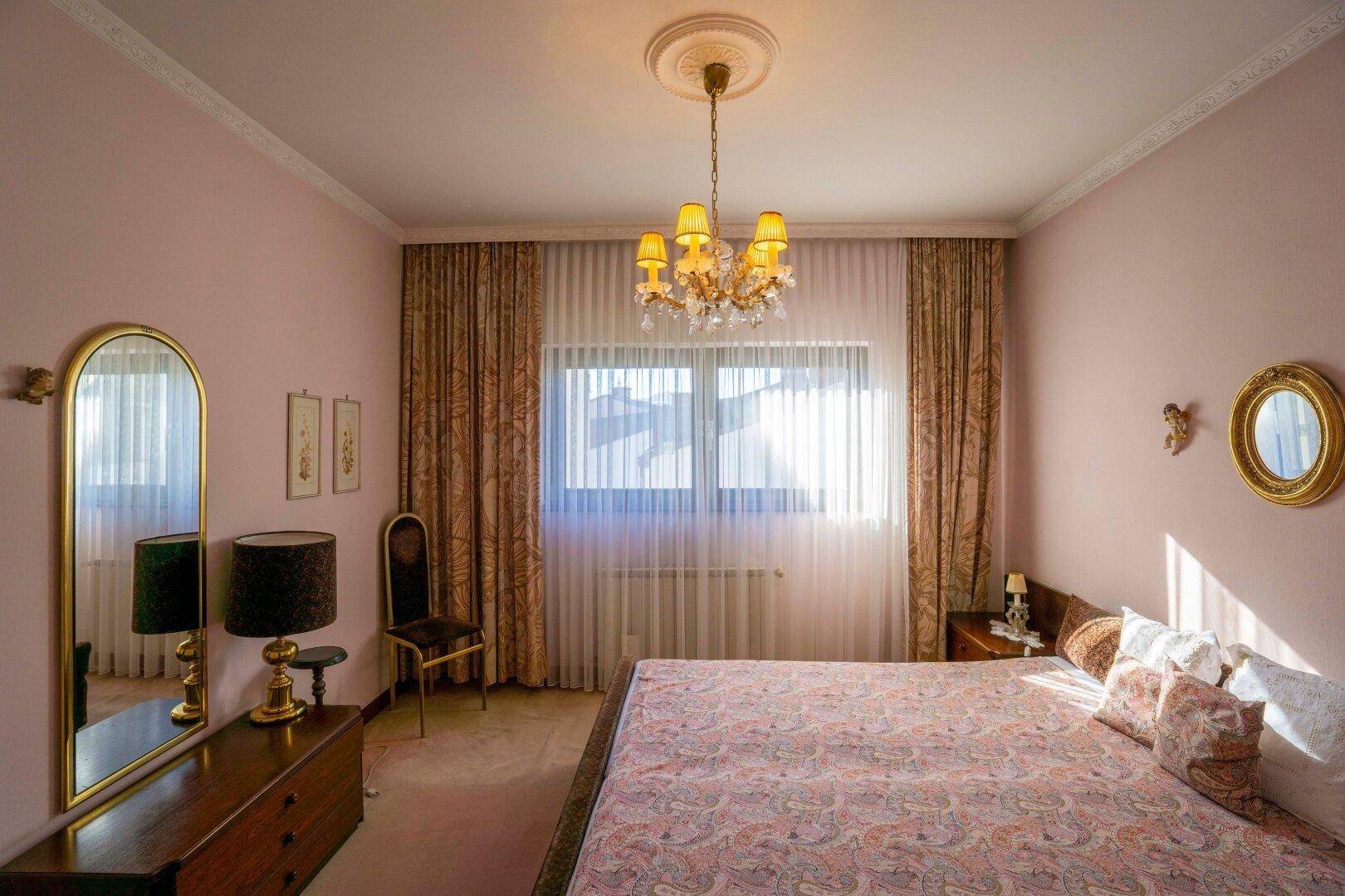 Geräumiges Schlafzimmer mit Doppelbett, Teppichboden und Kronleuchter an der Decke.