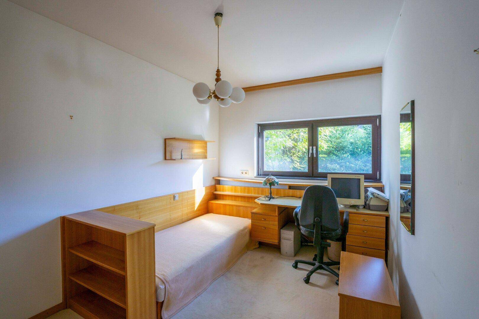 Helles Schlafzimmer mit Einzelbett, Schreibtisch und Fenster mit Blick ins Grüne.