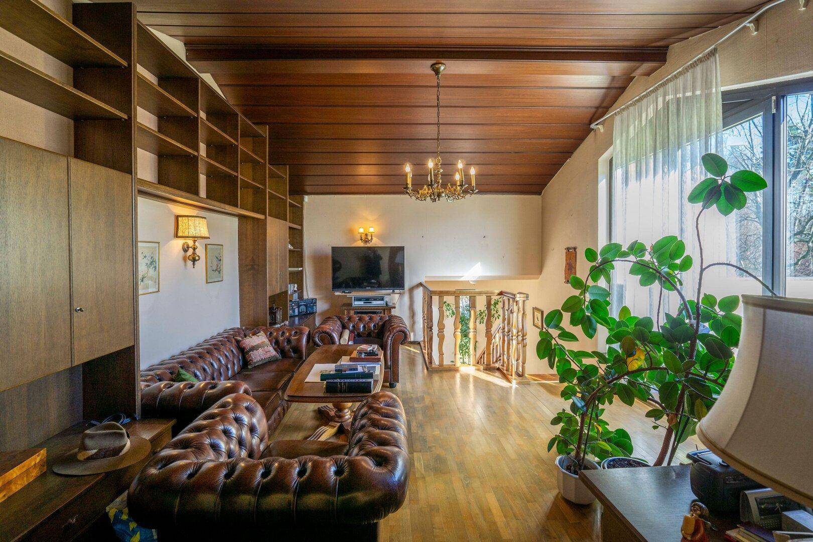 Wohnzimmer mit Holzbalkendecke, Einbauregalen und Ledersofas in rustikalem Stil.