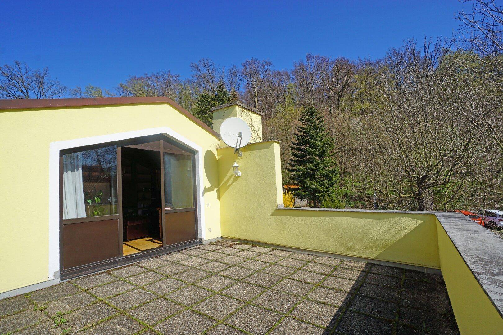 Große Dachterrasse mit Fliesenboden und weitem Blick auf die bewaldete Umgebung.