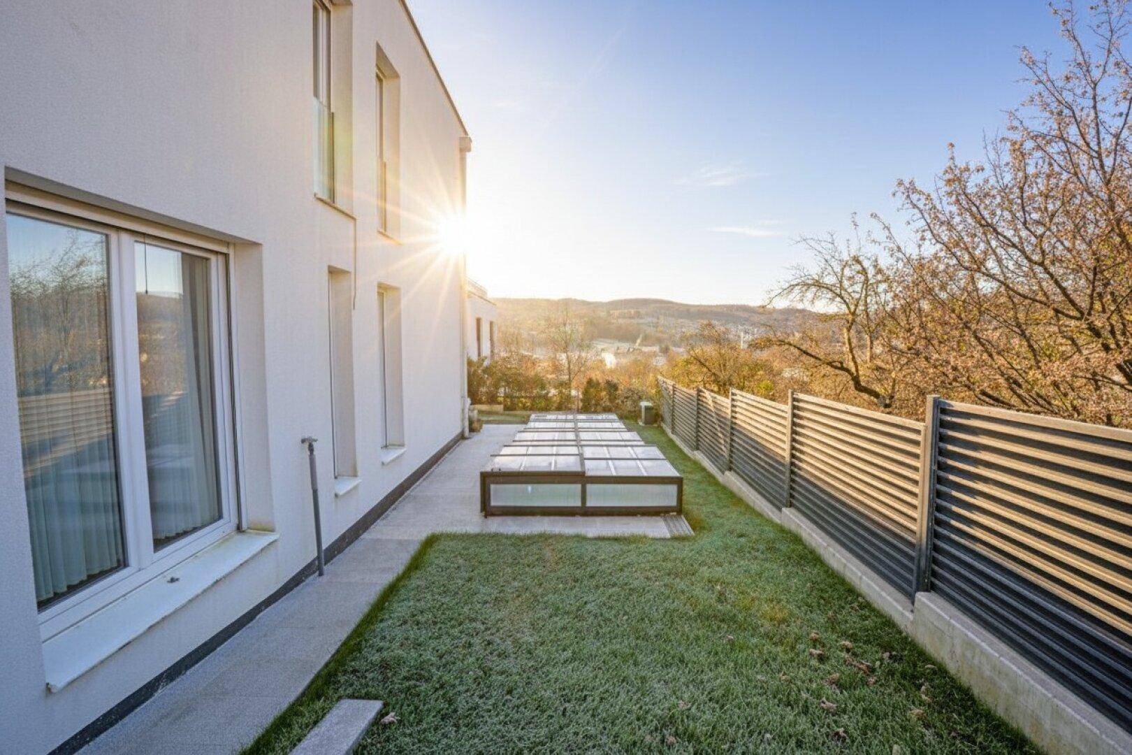 Sonnige Rasenfläche entlang der Hauswand mit Blick auf die umliegende Landschaft.