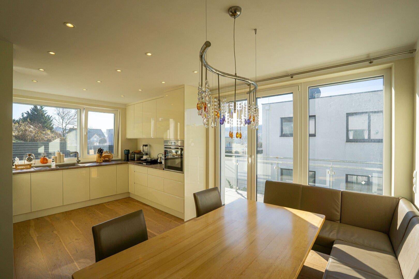 Helle, moderne Wohnküche mit glänzenden Schränken, Esstisch und großen Fenstern.