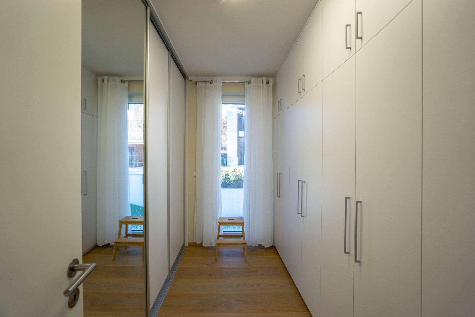 Praktischer begehbarer Kleiderschrank mit vielen Einbauschränken und Fenster.