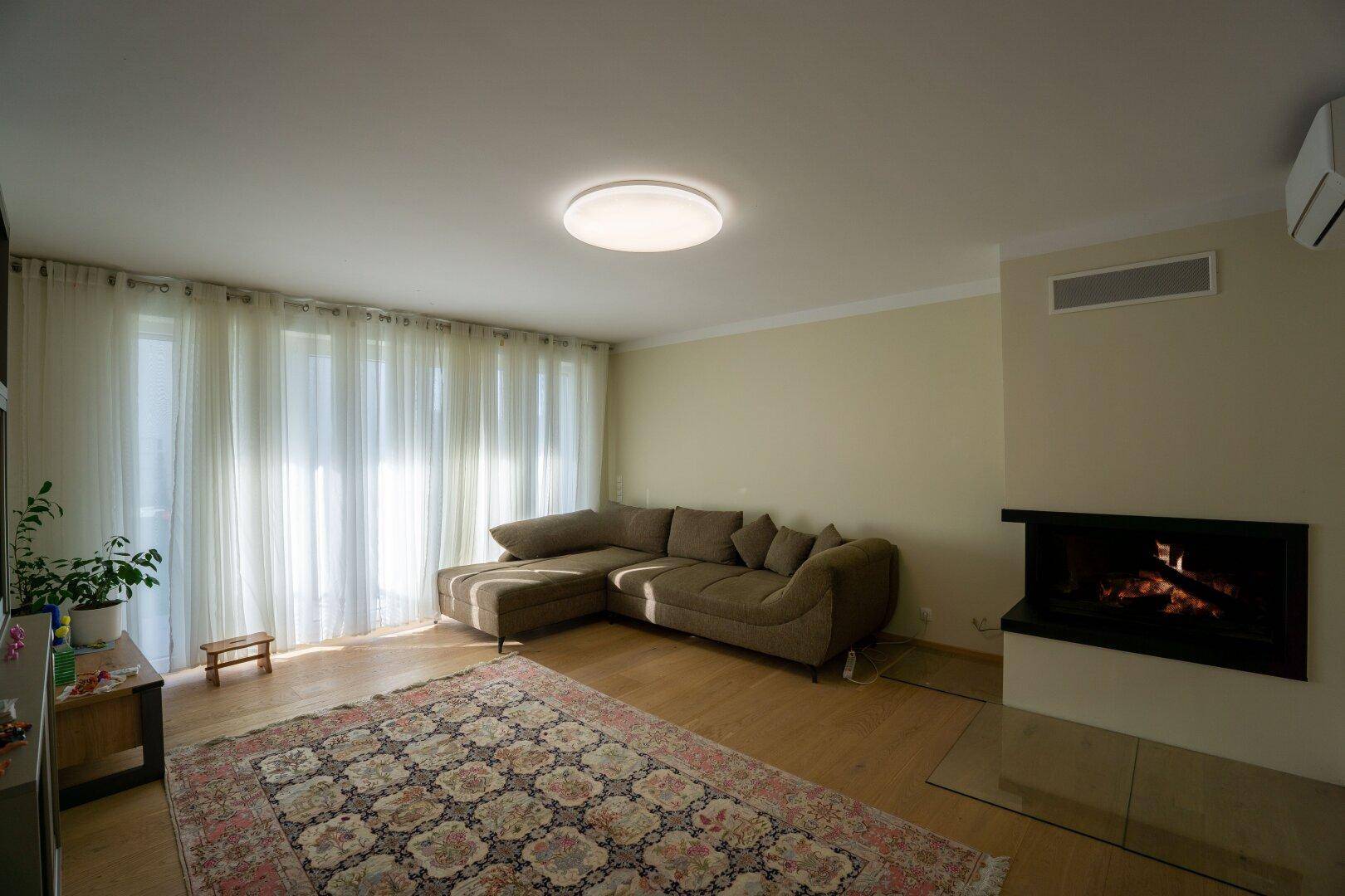Geräumiges Wohnzimmer mit beigem Sofa, Kamin und hellem Parkettboden.