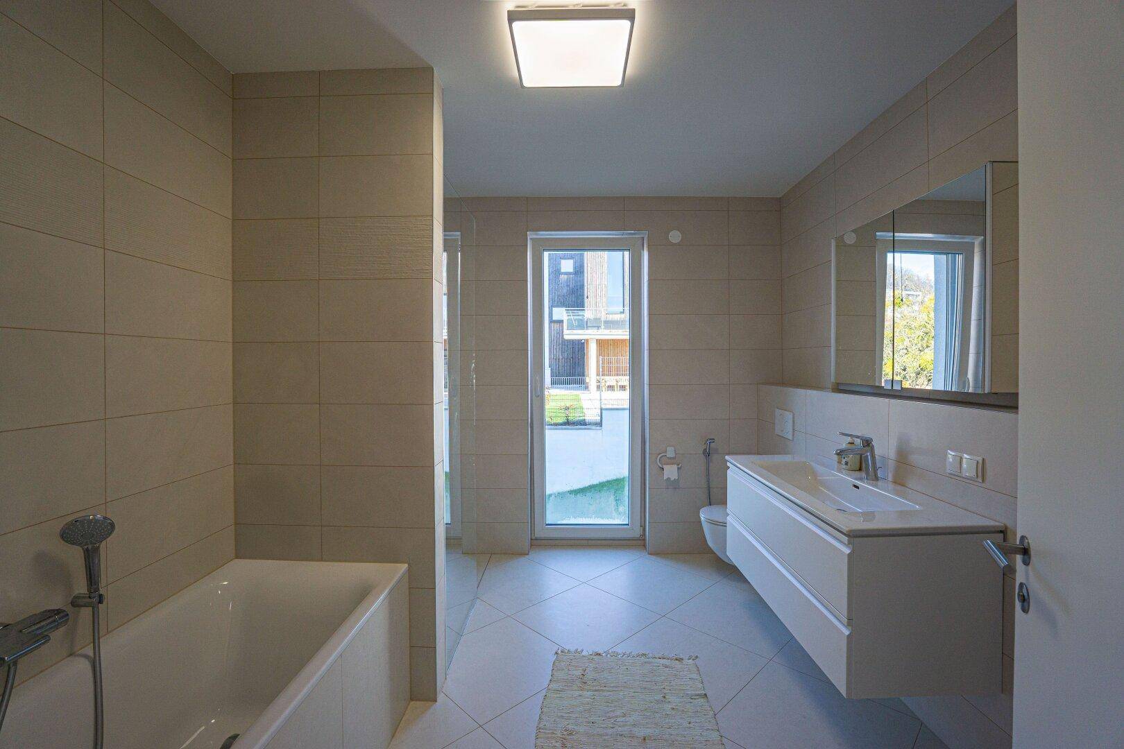 Modernes Badezimmer mit Badewanne, großformatigen Fliesen und Fenster zum Garten.