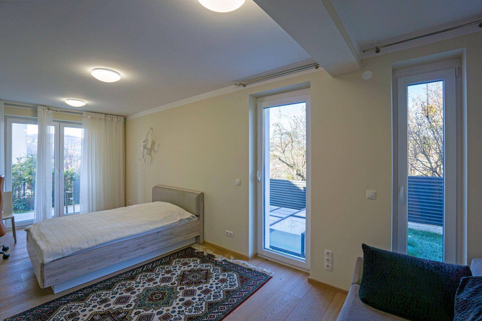 Helles Schlafzimmer mit Einzelbett, Holzboden und Zugang zu einem Außenbereich.