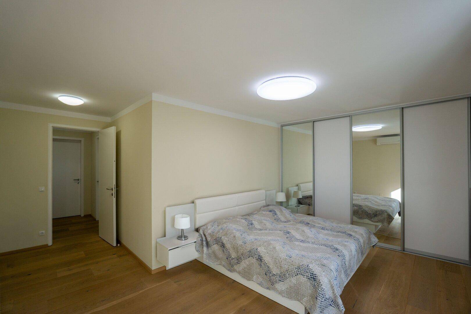 Geräumiges Schlafzimmer mit Doppelbett, Parkettboden und großen Spiegelschränken.