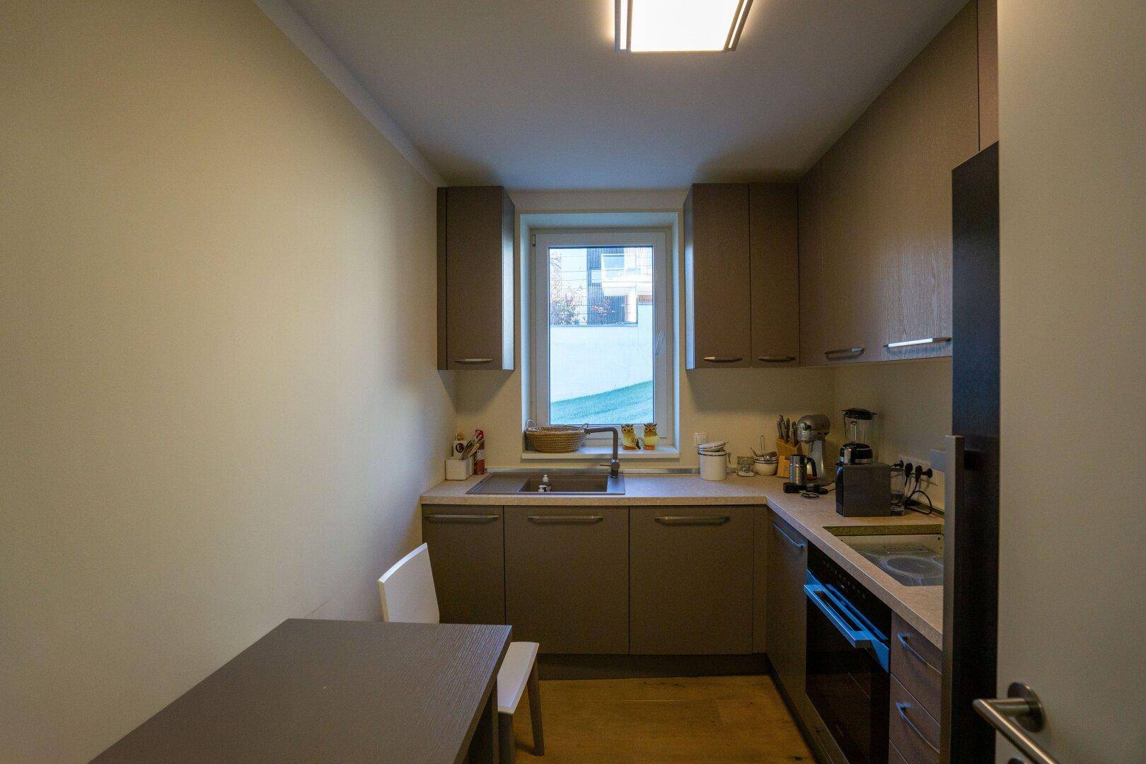 Kompakte Küche mit braunen Schränken, Fenster und kleinem Essbereich.