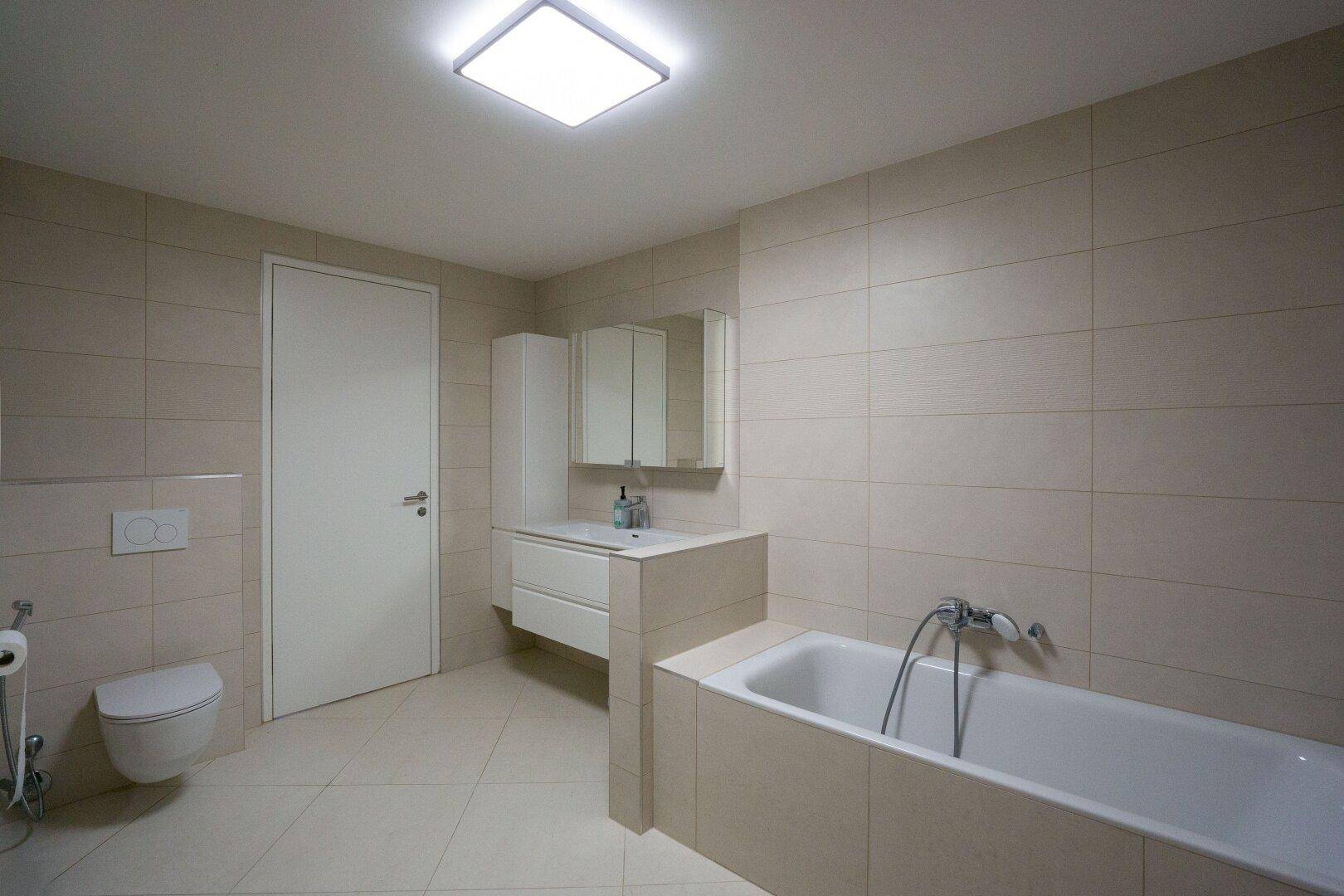 Modernes Badezimmer mit Badewanne, Wand-WC und großformatigen Fliesen.